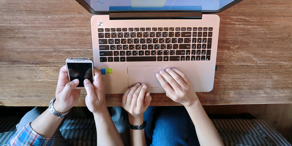 hands holding iPhone and hands on laptop